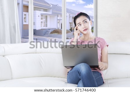 Casual woman sitting on the cozy sofa at home while using a laptop and looking up