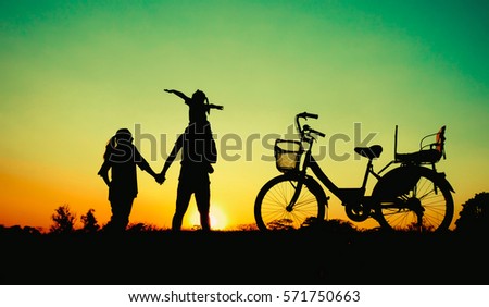 Silhouette happy family father,mother and daughter with bicycle in the park at sunset