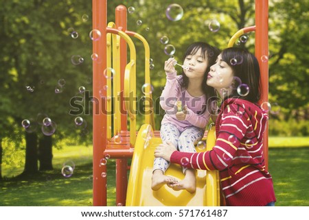Photo of a beautiful mother and her daughter blowing soap bubbles on the playground at the park