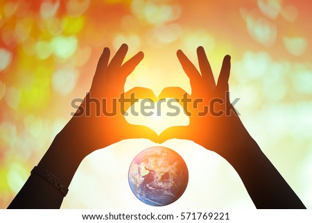 Hands in shape of love heart. Female door hands in the form of heart against the earth and blurred pass sun flare. Healthcare and Valentine's day concept. Elements of this image furnished by NASA.