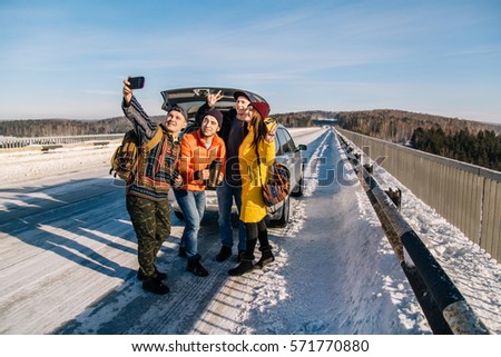 The company of young people traveling by car on winter road. Stopped to take a pictures of themselves.