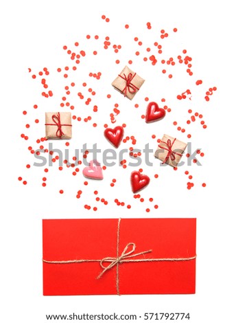 Styled Valentines Day flatlay top view. Red envelope tied with rope, hearts sweets, presents and confetti. Holiday concept