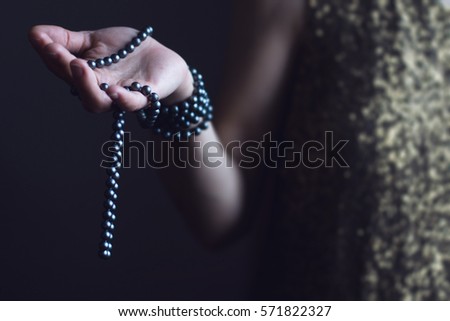 close up of a Caucasian retro woman in gold sequin vintage dress holding a necklace of black pearls with her hands on dark background