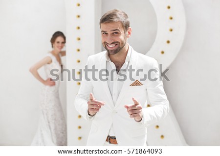 Chic wedding couple groom and bride posing in a white Studio. Happy couple laughing. White dress. White suit. Youth. Wedding. Chandelier. Sofa. The door.