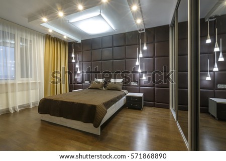 Contemporary Master bedroom In a luxurious apartment downtown. Modern designer materials. Soft brown palette. Sophisticated lightning. Brown bed linen, brown pillows. Golden curtains. Big windows. 