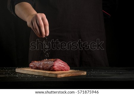 Beef steak and salt by chef on the background with free space for text design or logotype menu restaurant. Horizontal photo. Food background. Black text area.