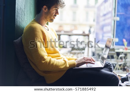 Stylish male freelancer working on new startup project making internet researchers analyzing data using laptop computer and wireless connection to 4G internet in city cafe with free wireless zone