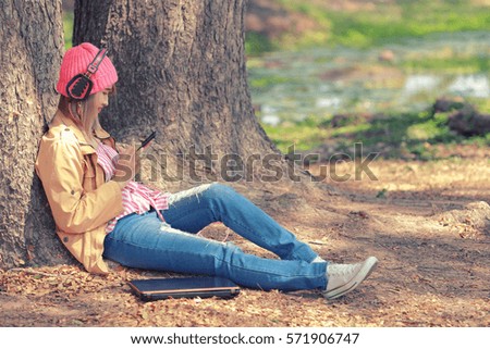 Happy and stylish hipster woman take pictures and listen to music from a mobile phone in the park.Vintage color.
