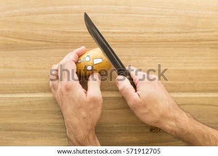 a fresh potato with cartoon style face scared to death while being held in one hand. The other hand holds a big knife