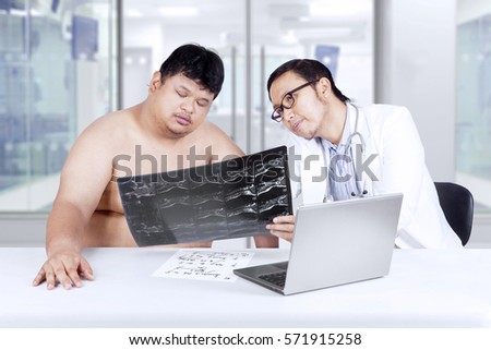 Picture of Asian doctor showing x-ray result at overweight patient in the hospital