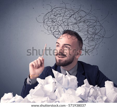 Young businessman sitting behind crumpled paper with scribbles over his head