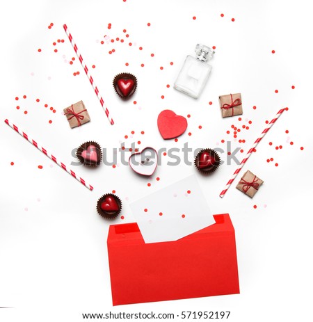 Styled photo of Valentine's Day flatlay top view isolated on white. Red heart sweets, gifts in craft paper, proposal ring in box, red envelope with empty note, perfume and confetti. Party invitation