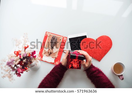 Close-up of the female hands opening a present on white background. Flowers, cup, card and heart on table. Valentine's Day, Love, Birthday, Holidays concept. Isolated