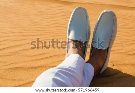 Relaxation. Mans legs/feet lying on the hot desert sand. Royalty-Free Stock Photo #571966459