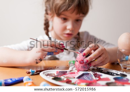 Little girl painting Easter eggs with paintbrush