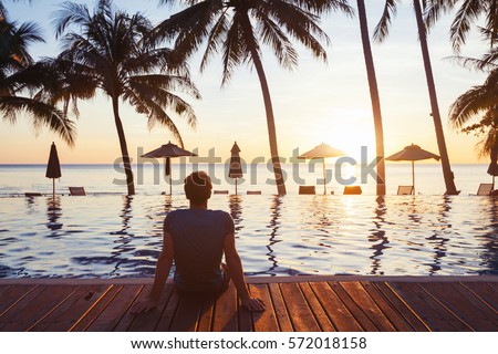 relaxation on the beach, young man enjoying beautiful sunset in luxury hotel near swimming pool Royalty-Free Stock Photo #572018158