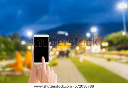 woman use mobile phone and blurred image of people in the park in the evening with beautiful bokeh from the lights