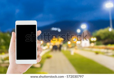 woman use mobile phone and blurred image of people in the park in the evening with beautiful bokeh from the lights