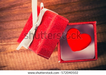 Love concept. Decorative red heart in nice red gift box on wooden background.