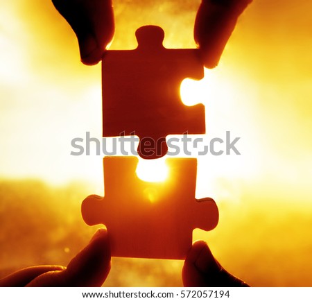 two hands trying to connect couple puzzle piece with sunset background. Jigsaw alone wooden puzzle against sun rays. one part of whole. symbol of association and connection. business strategy.