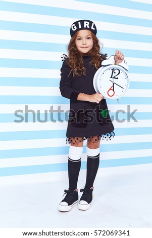 Beautiful cute pretty little girl baby blond curly hair fun to play children room party striped background wear dress style fashion clothes winter collection watch alarm Alice in Wonderland daughter.