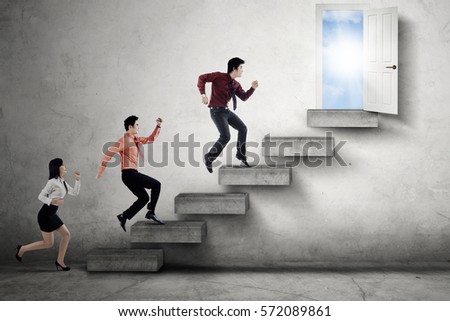 Three young businesspeople running on the stairs and compete to reach an opportunity door to success