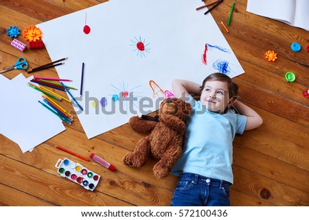 girl lying on the floor with a teddy bear. Girl lying on the floor among the paints and pencils
