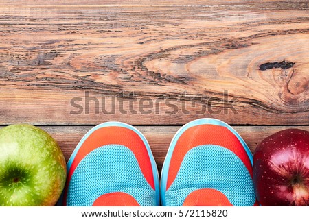 Green and red aplles. Sneakers on wooden surface. Sport makes your life healthy.