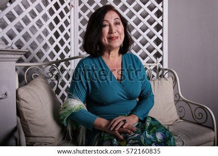 Mature Asian woman sitting on couch in luxurious dress