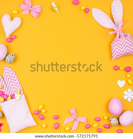 Stylish background with decoration: pink and yellow Easter eggs, fabric bunny gift bags with candies.  Kids concept. Flat lay