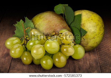 A bunch of green grapes (Muscat 'Italia'), and two organic apples (Reine de Reinettes) with leaves, on a rustic wooden background.
