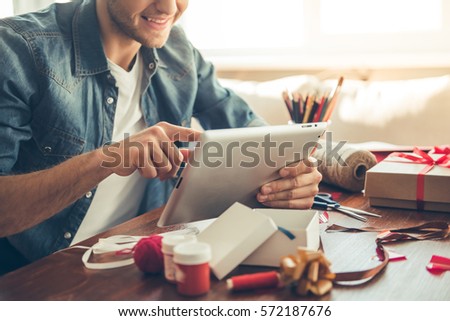 Cropped image of handsome romantic guy using a digital tablet and smiling while making present for his couple