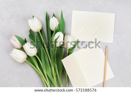 Spring tulip flowers and paper card on gray stone table from above in flat lay style. Greeting for Womens or Mothers Day