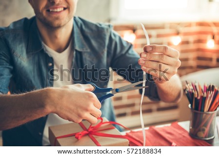 Cropped image of handsome romantic guy smiling while making present for his couple
