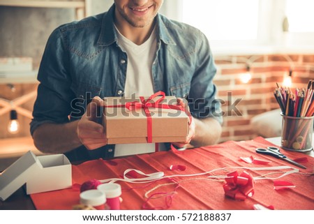 Cropped image of handsome romantic guy smiling while making present for his couple