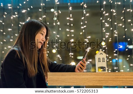 Beautiful asian woman long brown hair with winter coat holding a smartphone looking down the screen in resturant with bokeh background, technology, communication concept
