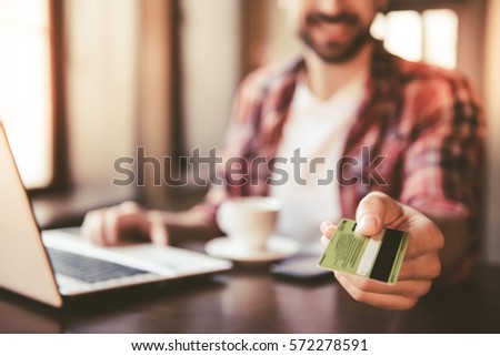 Handsome man is giving a credit card and smiling while working with a laptop in cafe