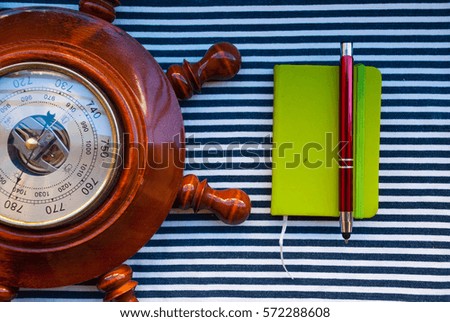Barometer wheel with green notebook and pan on striped fabric. Man sailor set. Top view.