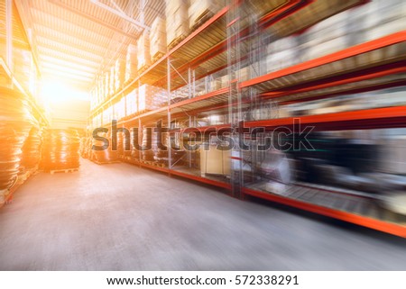 Warehouse industrial and logistics companies. Commercial warehouse. Boxes and crates stocked on the shelves of three storey. The effect of motion blur. Bright sunlight. Royalty-Free Stock Photo #572338291