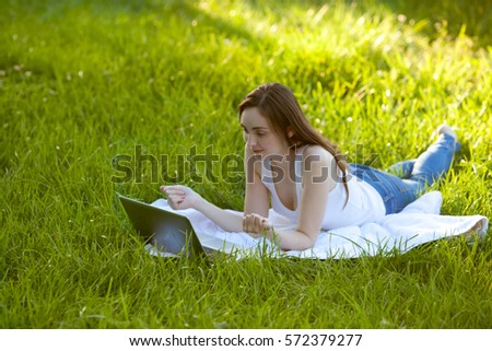 Woman with laptop relaxing lying on green grass