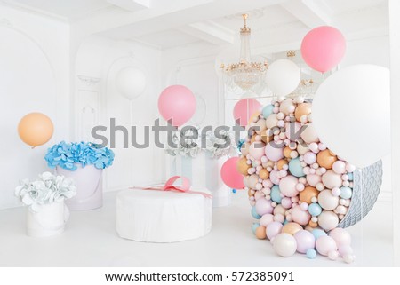 Boxes with flowers and a large pudrinitsa with balls and balloons in room decorated for birthday party.