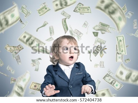 Portrait of a cute little baby boy wearing a suit and standing under a dollar rain against a gray wall. Concept of heritage.