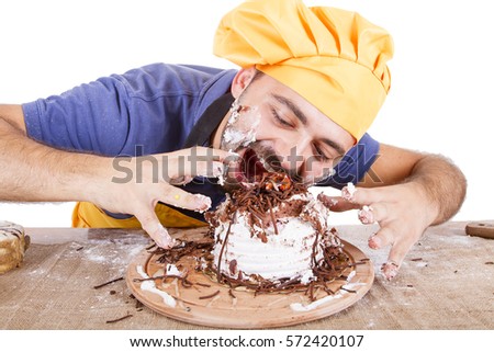 Picture of cheerful male chef in yellow uniform eating whole cake isolated on white background