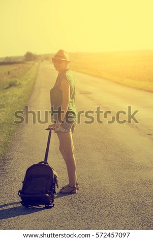 Woman with traveler bag on the highway in summer sunset