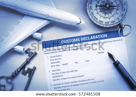 Blank or empty customs declaration form put on a wood table, decorated with a white model airplane, two vintage brass keys, a compass and a fountain pen. Every travelers must fill and sign this form.
