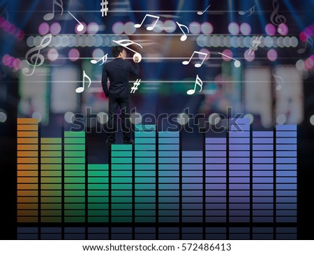 Businessman standing over the sound waves equalizer and drawing the  music note on photo blurred of stage background,musical concept