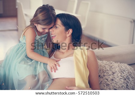 Pregnant woman and her little daughter enjoying at home. 