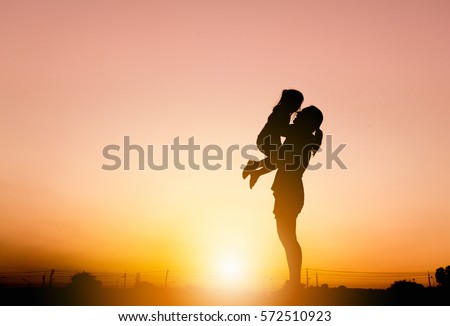 Silhouettes of mother and daughter playing at sunset evening sky background. Royalty-Free Stock Photo #572510923