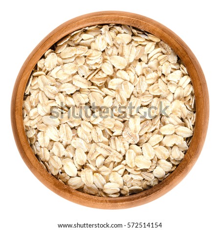 Oatmeal, rolled oats in wooden bowl. Dehusked, hulled oats, rolled into large whole flakes. Porridge oats, used in granola or muesli. Isolated macro food photo close up from above on white background. Royalty-Free Stock Photo #572514154