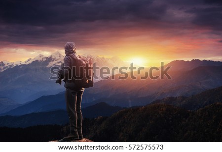 Professional photographer takes photos with big camera on peak of rock. Dreamy majestic landscape, sunset color